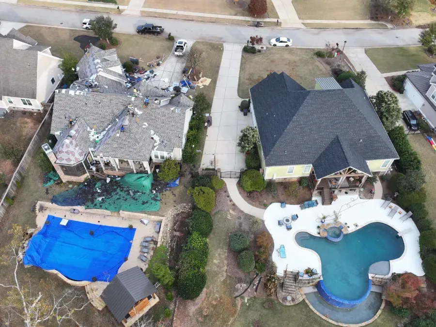 Aerial view of two suburban homes, one with a blue-covered pool and one with a freeform pool.