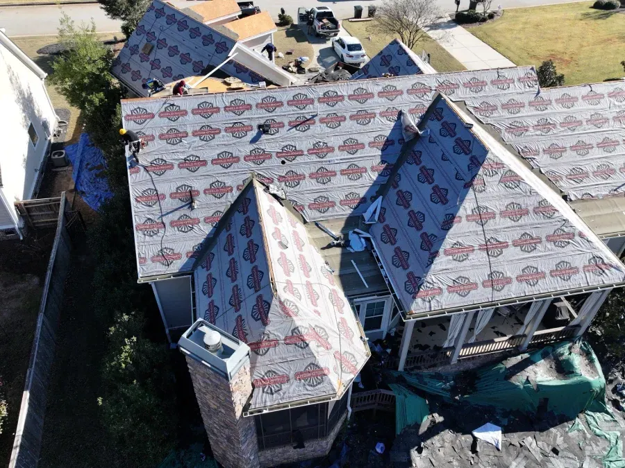 Damaged house roof with exposed underlayment and debris after storm damage