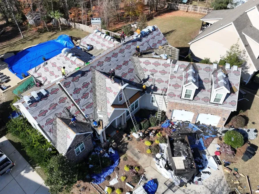 Aerial view of a house with a partially replaced roof and construction materials around it.