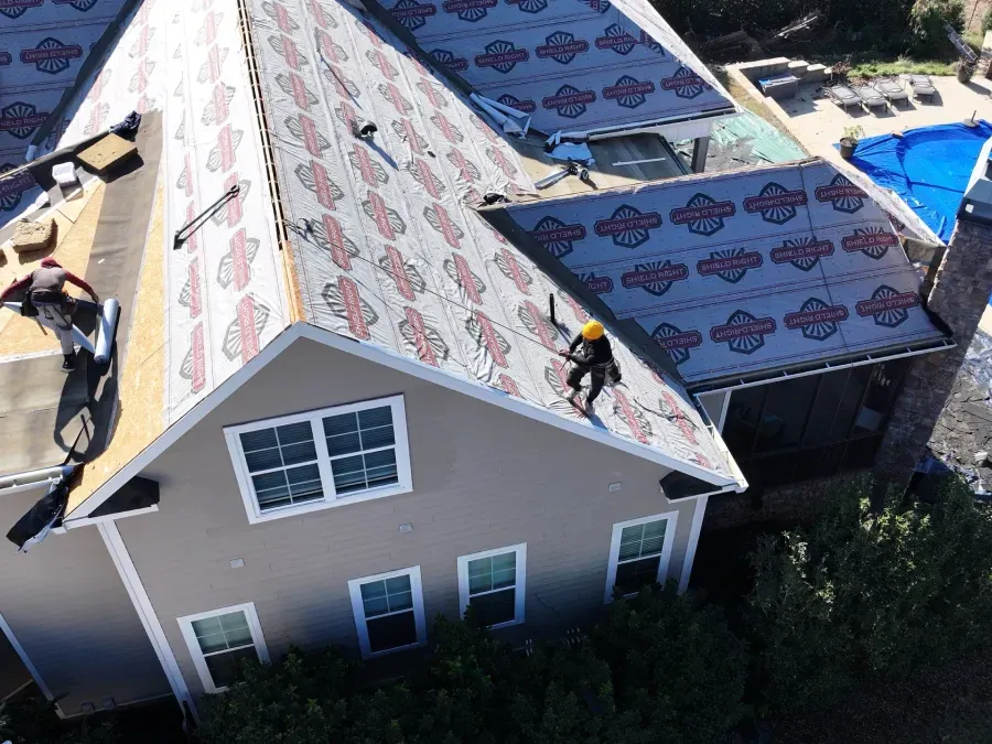 Roofers working on a house roof with underlayment and shingles during repair.