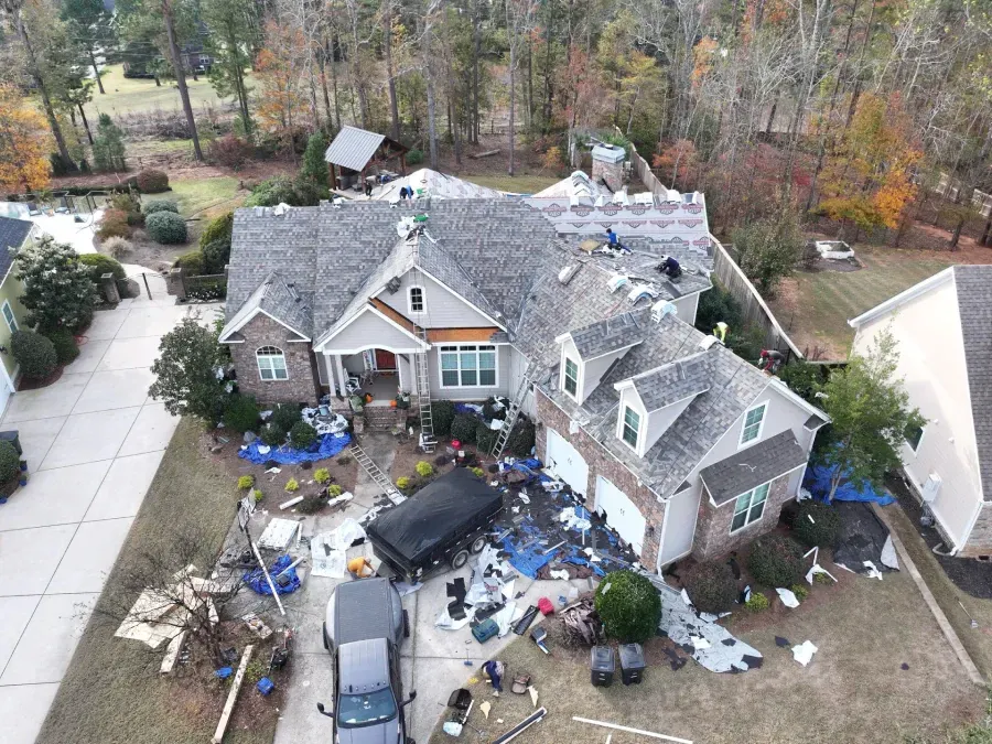 Aerial view of a house with extensive roof damage and debris scattered across the yard and driveway.