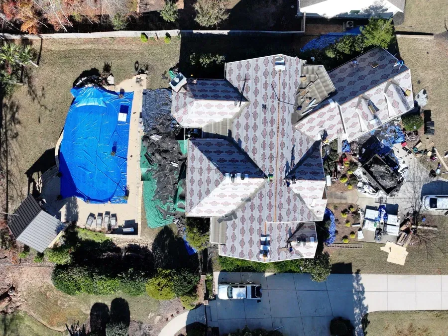 Aerial view of a house with a gray roof, blue swimming pool, and patio area in a residential yard