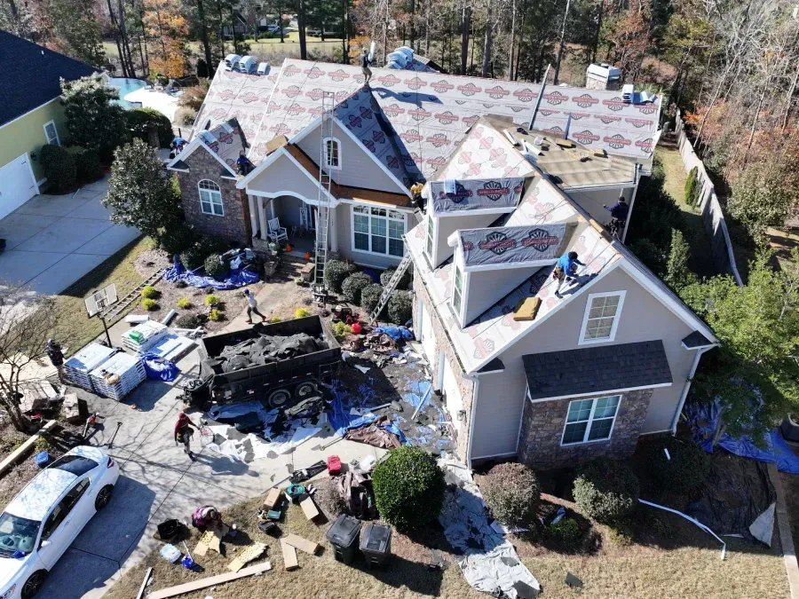 Damaged house with torn roof, debris, and a blackened front yard after a fire or storm