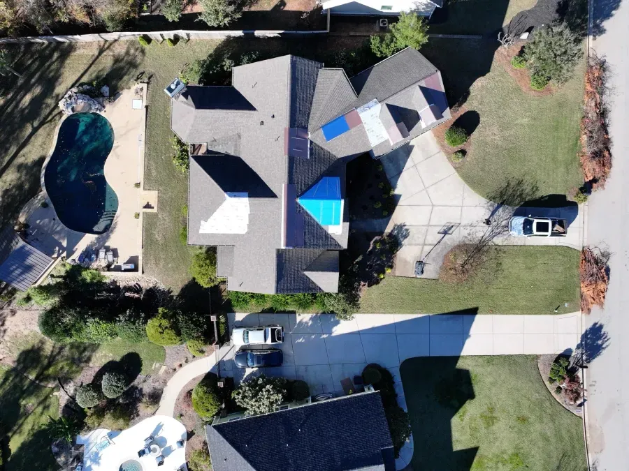Aerial view of a suburban home with a pool, driveway, parked cars, and patio umbrellas