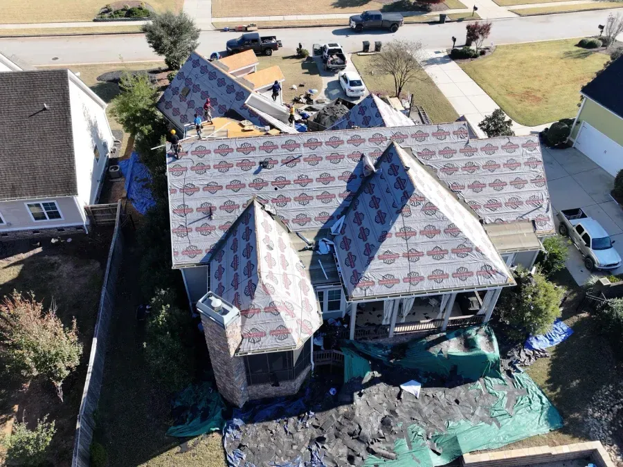Aerial view of a house with a patterned roof, construction materials, and tarps around it