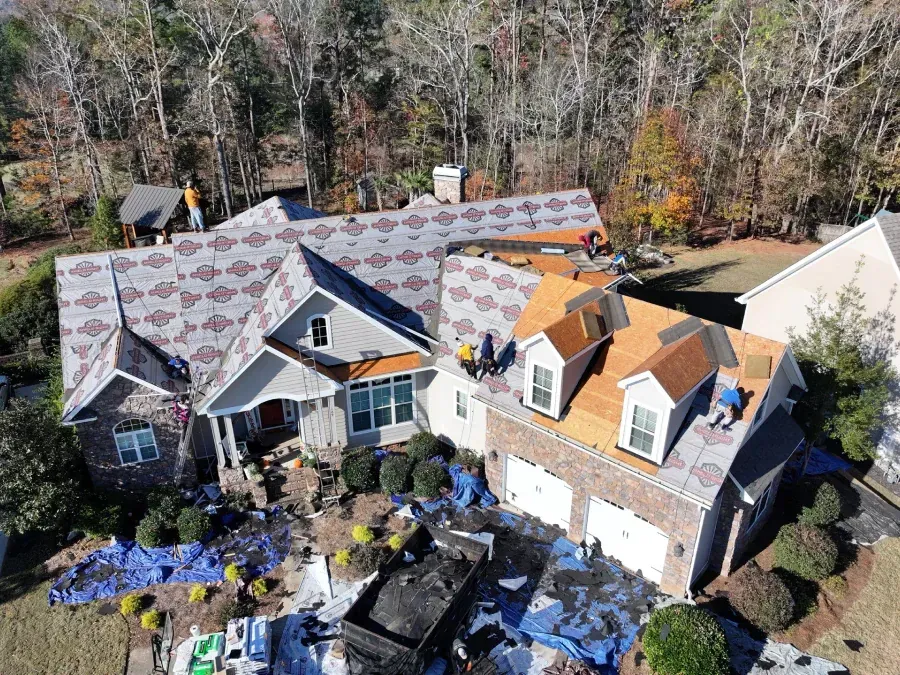 Aerial view of a house under roof repair with blue tarps and scattered shingles
