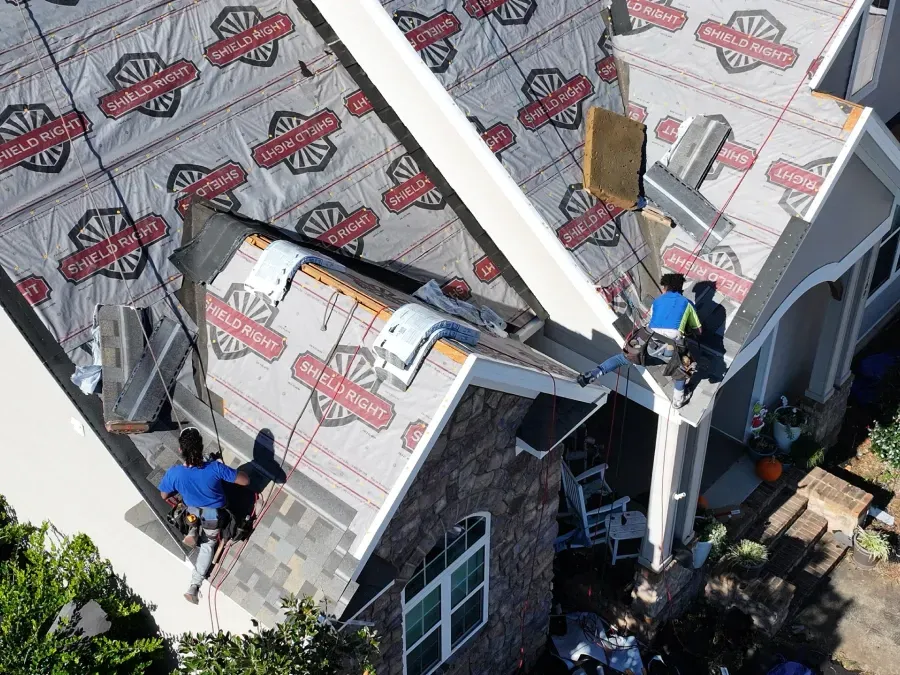 Workers on a roof installing white insulation boards on a house under construction