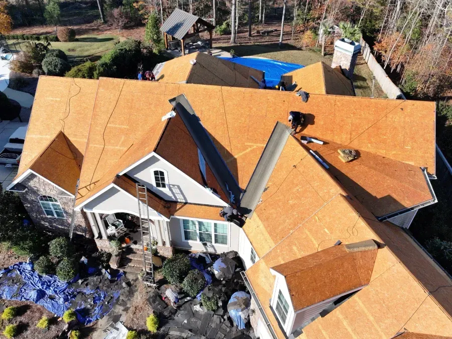 Aerial view of a house with a new orange roof being installed, surrounded by trees and landscaping