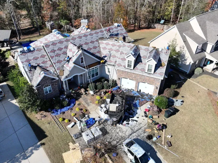 Aerial view of a house with roof damage and scattered debris in the yard after a storm