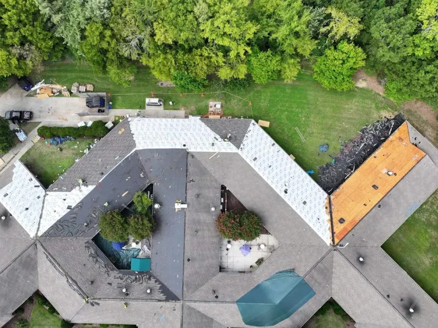 Aerial view of a modern courtyard house with gray roofs, patio areas, and a green lawn bordered by trees