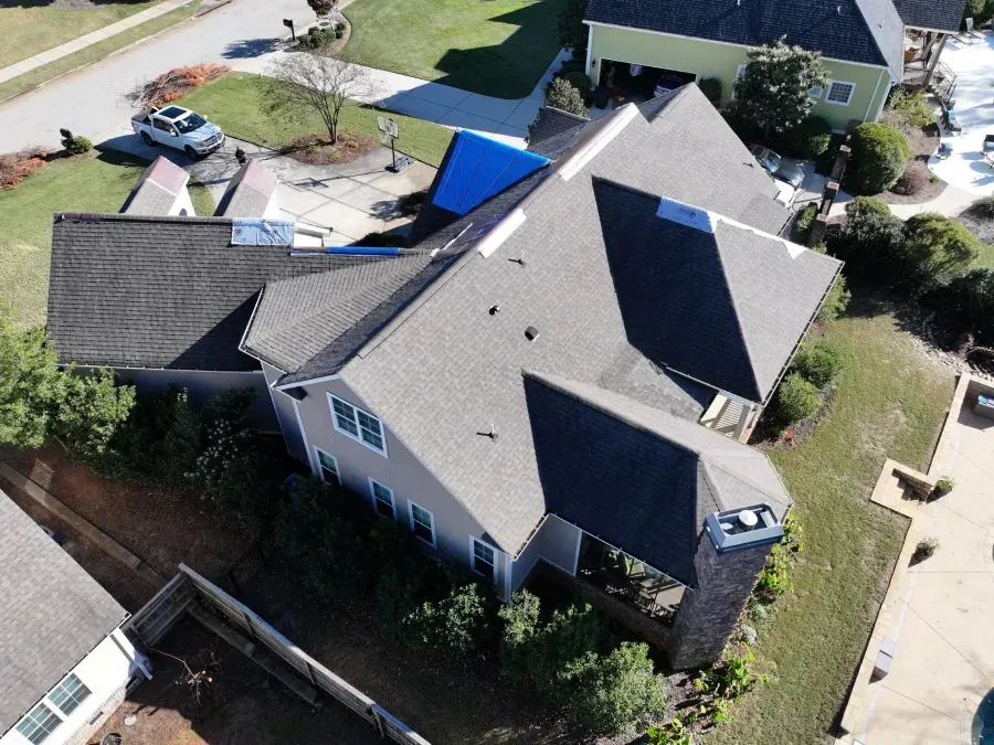 Aerial view of a suburban house with a gray roof, driveway, and surrounding yard.