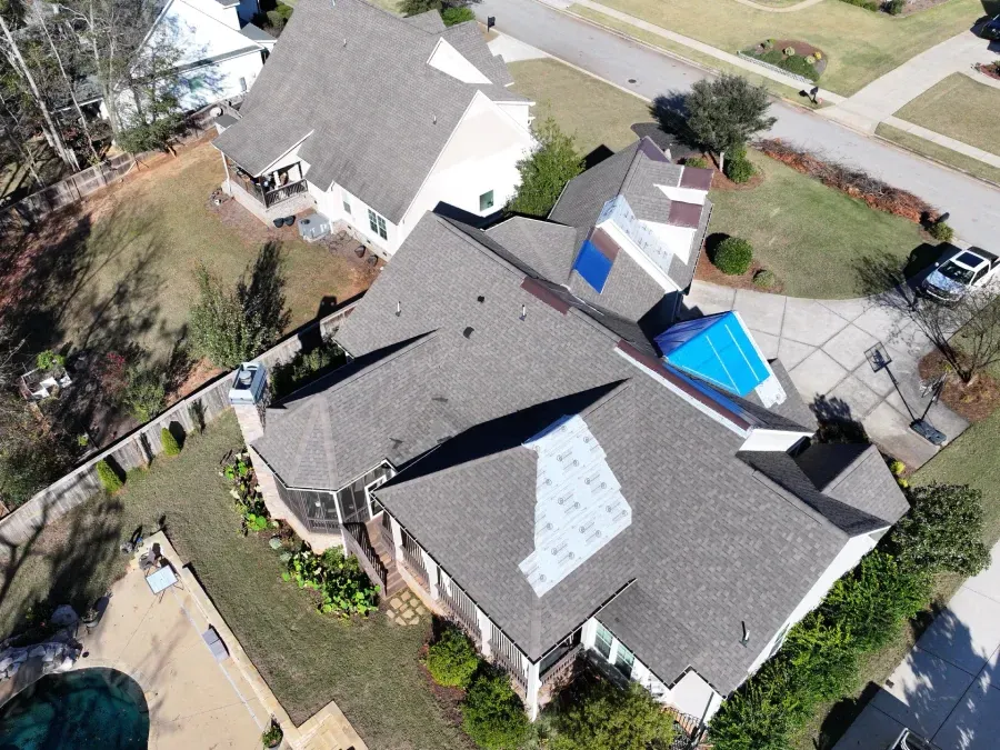 Aerial view of a house with gray roofs, a blue tarp, and a backyard fenced area.
