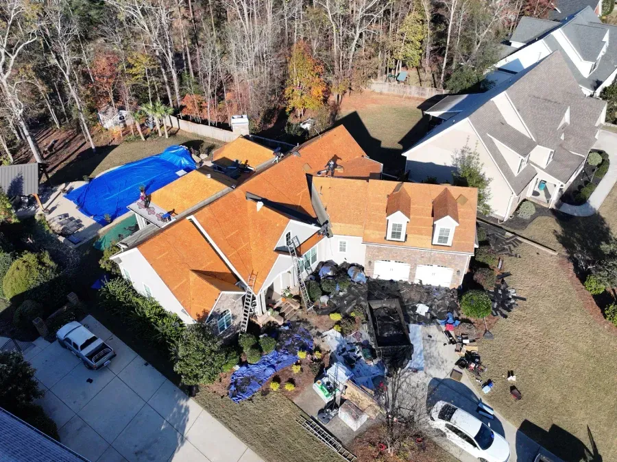 Aerial view of a house with orange roofs, blue pool cover, and parked cars beside wooded yard