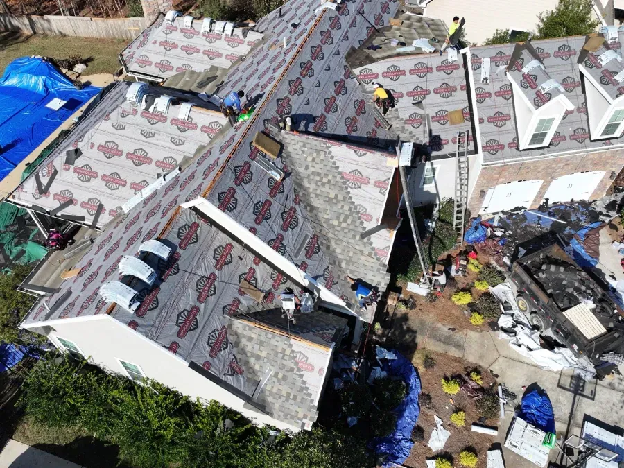 Aerial view of storm-damaged houses with torn roofs and debris scattered around the property