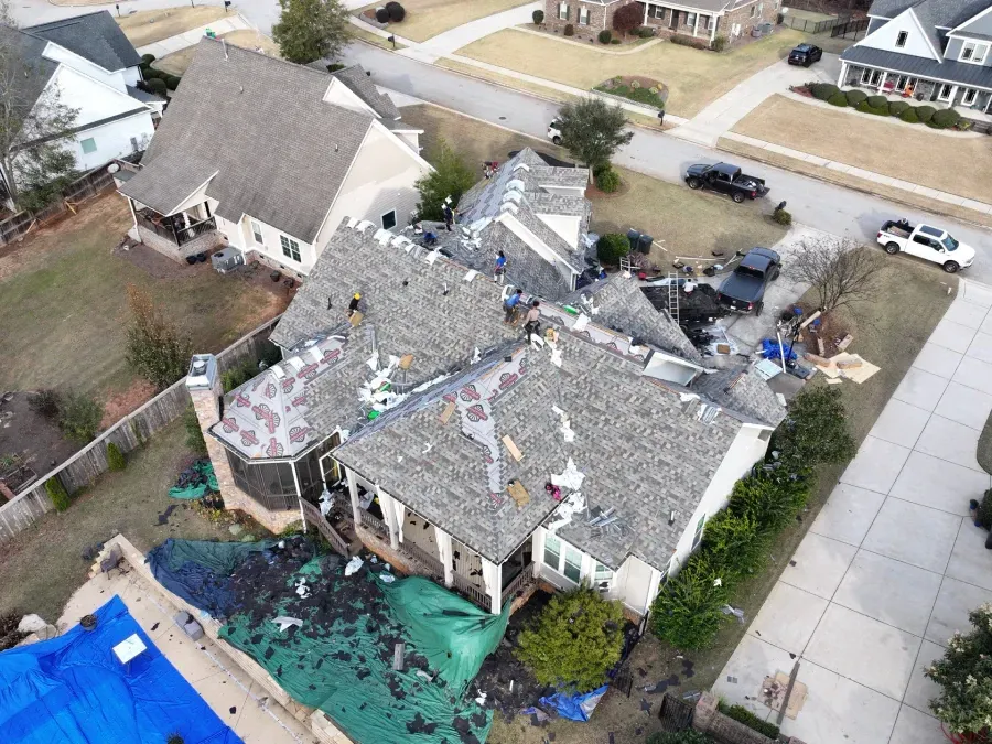 Aerial view of a storm-damaged house with a torn roof and debris scattered around the yard.