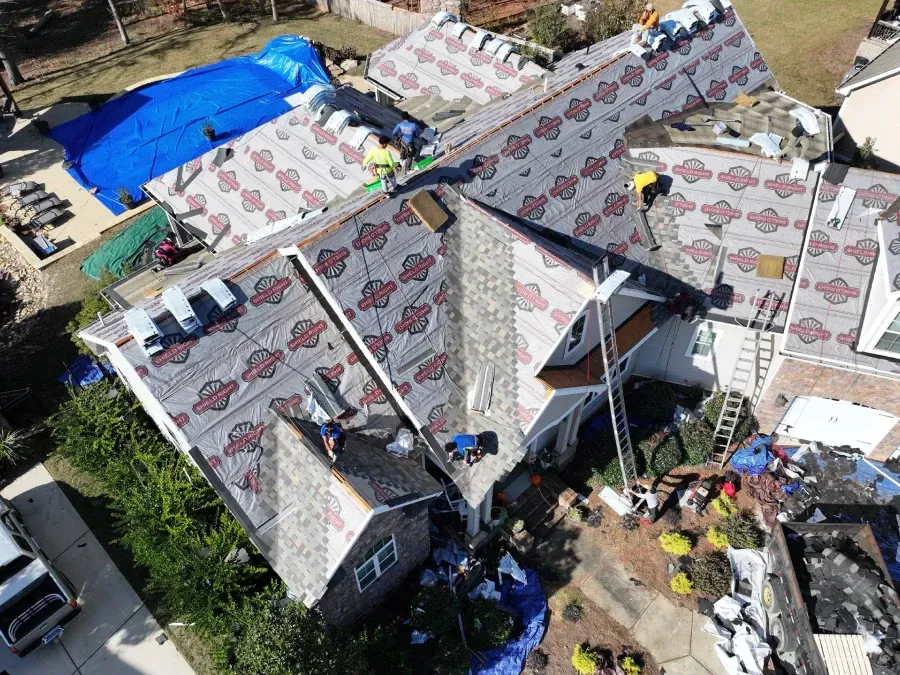 Aerial view of a damaged roof under repair with tarps, tools, and scattered debris around the house