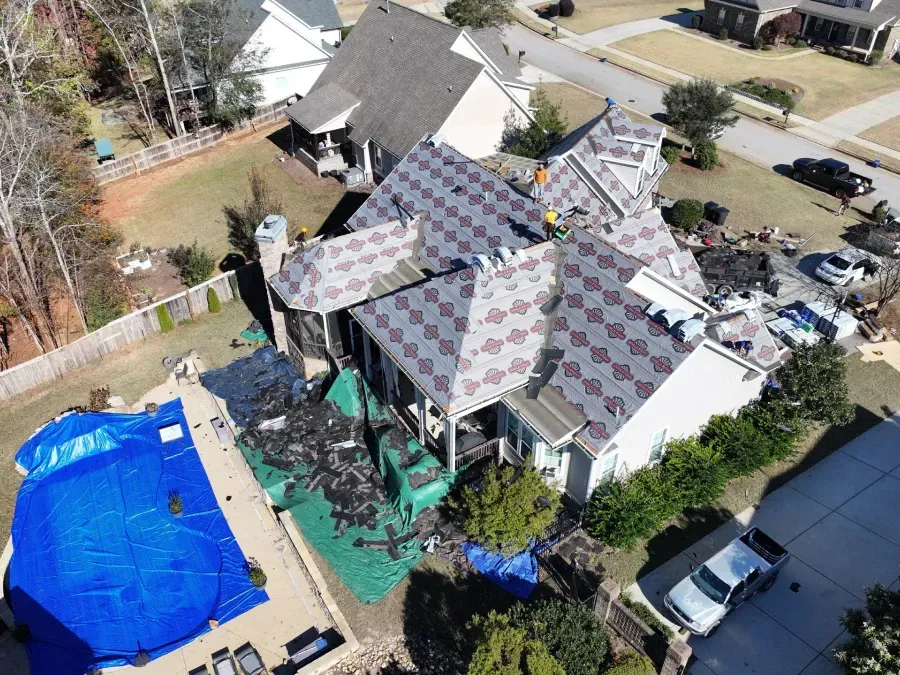 Aerial view of a house with a partially replaced roof, blue-covered pool, and materials around the yard.