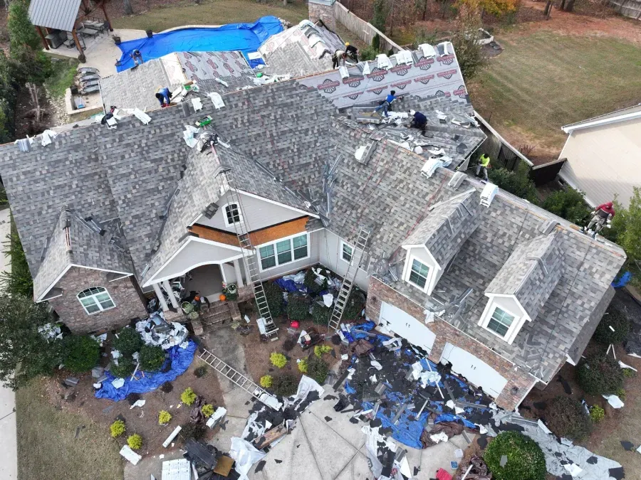 Aerial view of a storm-damaged house with missing roof shingles and debris scattered around the yard.