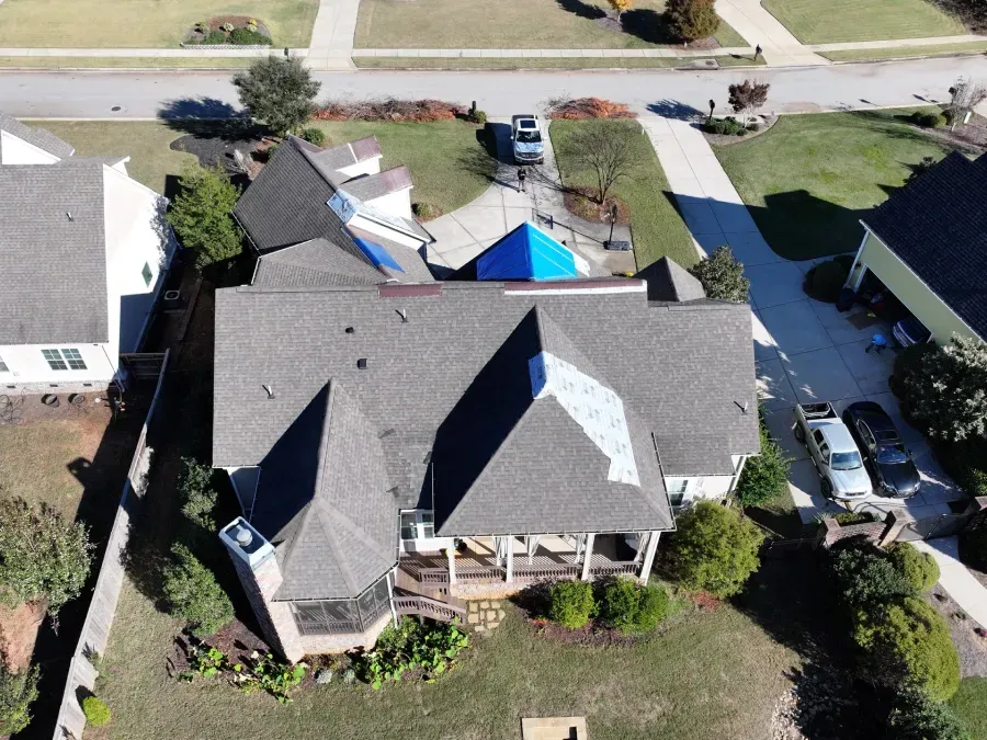 Aerial view of a large suburban house with a backyard pool and parked cars on a residential street.