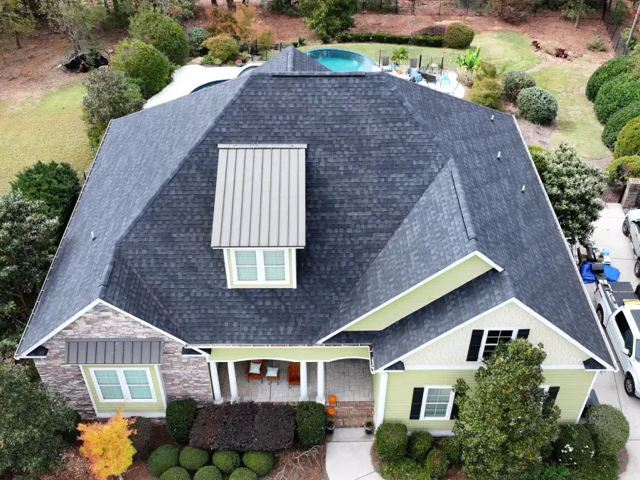 Aerial view of a house with a dark roof, dormer window, and landscaped yard.