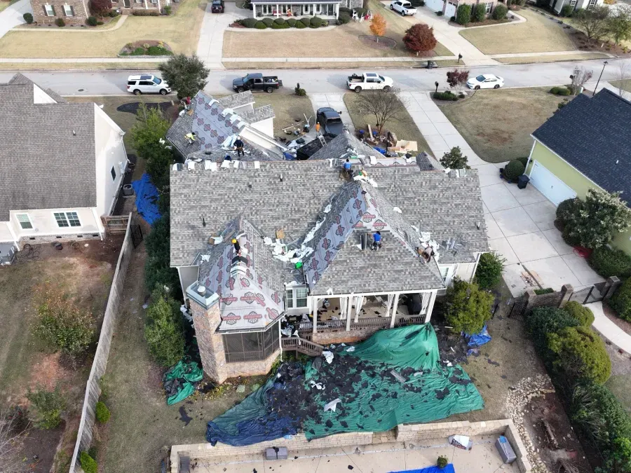 Aerial view of a house with severe roof damage and scattered debris after a storm.