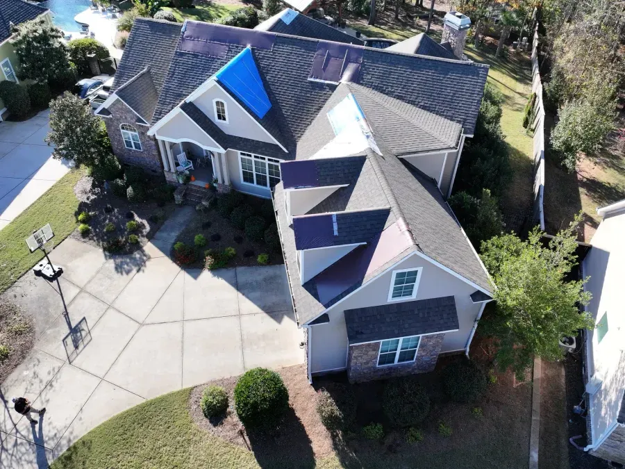 Aerial view of a suburban house with gray roofs, a blue dormer, and a large concrete driveway
