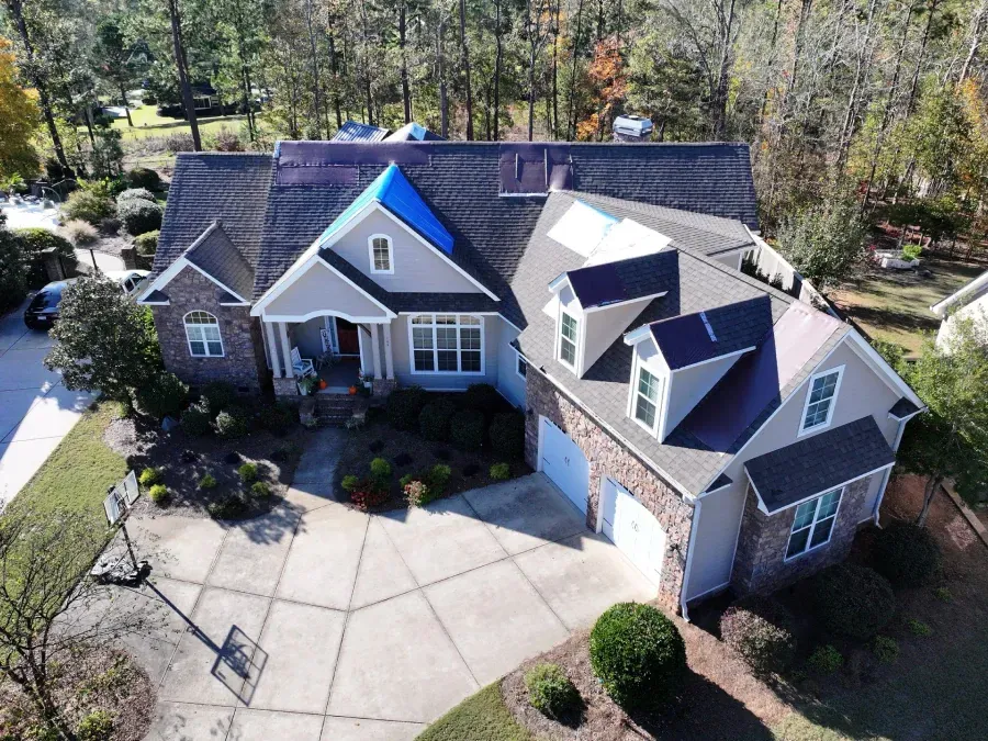 Aerial view of a large brick-and-gray suburban house with a driveway and trees around it