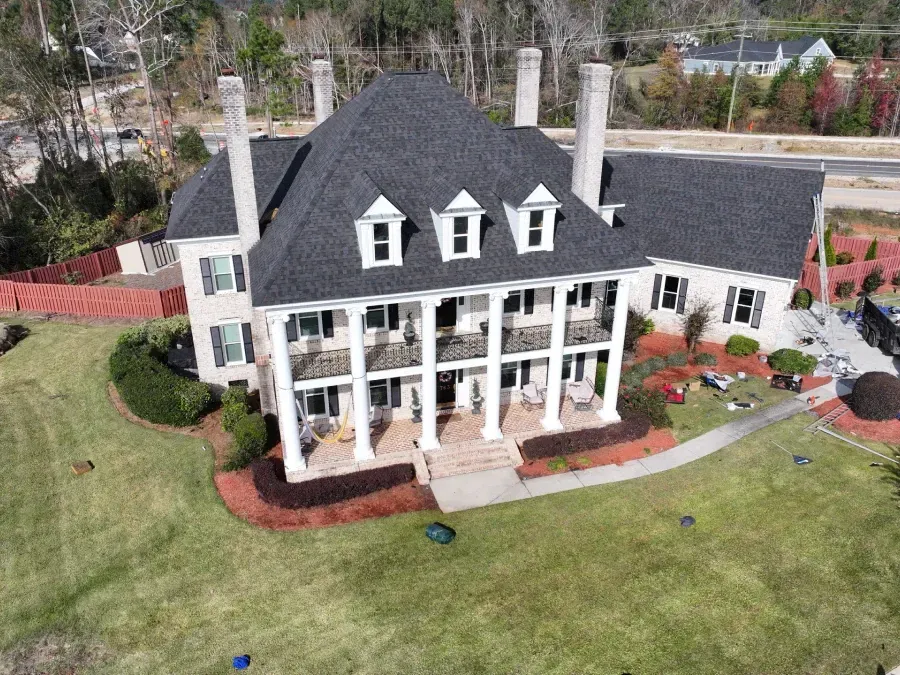 Aerial view of a large white house with a dark roof, wraparound porch, and landscaped lawn.