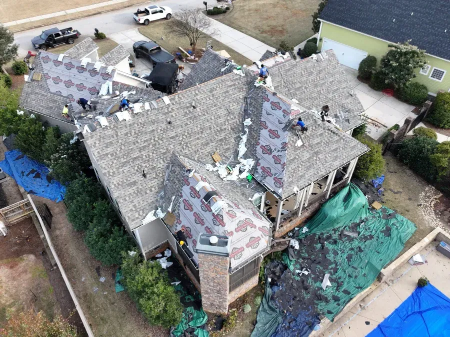 Aerial view of a house with workers repairing a damaged roof and debris-covered yard after a storm