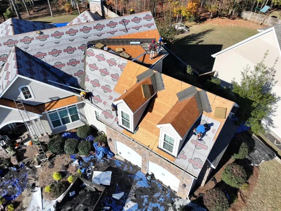 Aerial view of a house roof under repair with shingles, tools, and debris scattered below