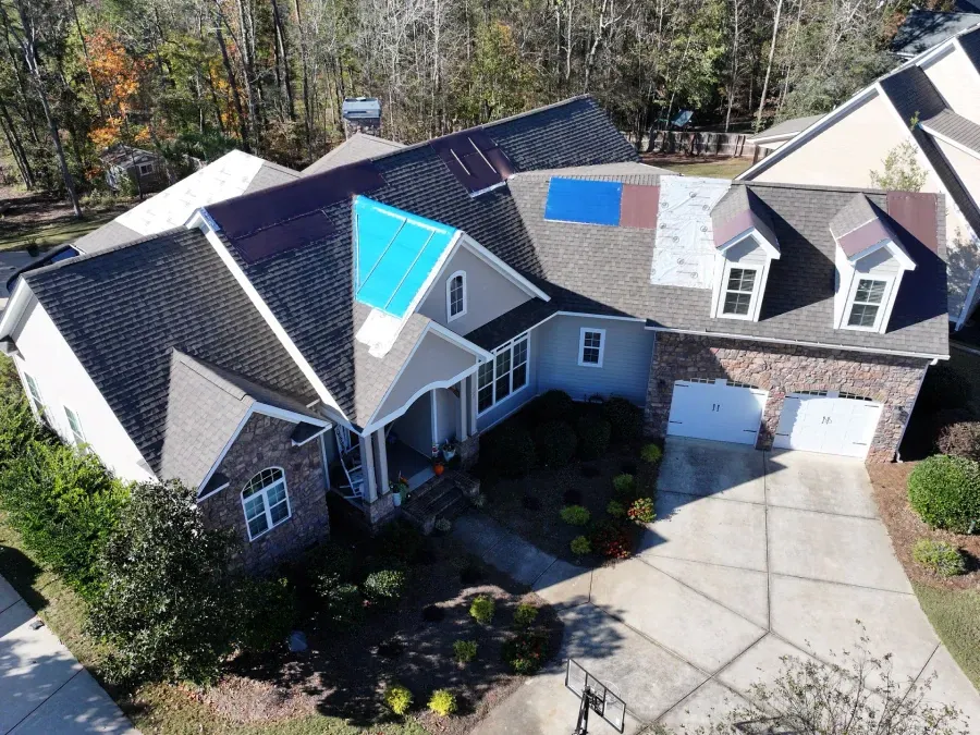 Aerial view of a suburban house with a blue tarp on the roof and a driveway in front