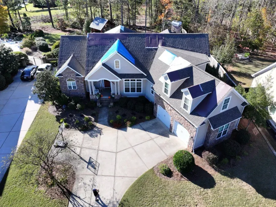 Aerial view of a large suburban house with gray roofs, blue front gable, and a circular driveway.