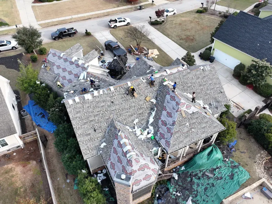 Damaged house roof with debris and tarp, seen from above in a residential neighborhood