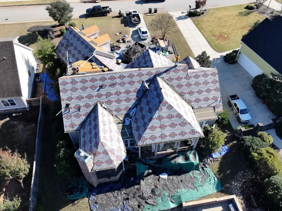 Aerial view of a house with partially replaced roof shingles and roofing materials in the yard