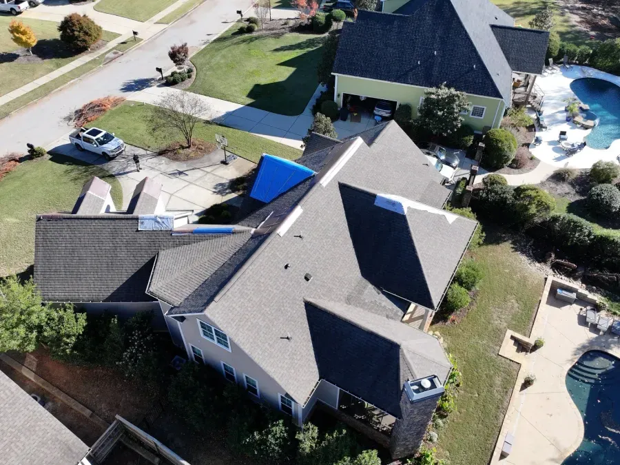 Aerial view of a suburban house with a gray roof, driveway, and a small backyard pool