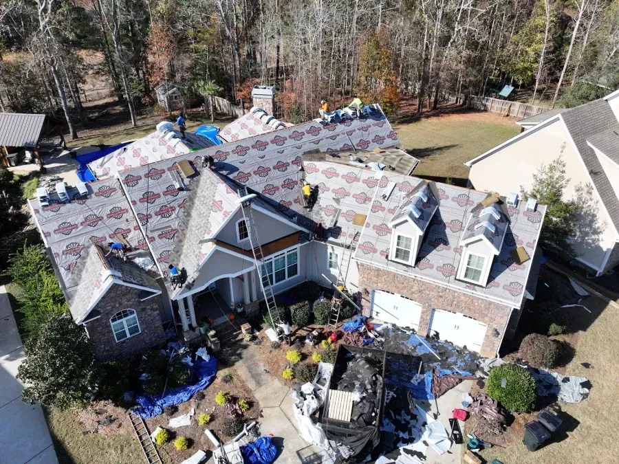 Aerial view of a house with a roof under repair, roofing materials scattered across the yard.