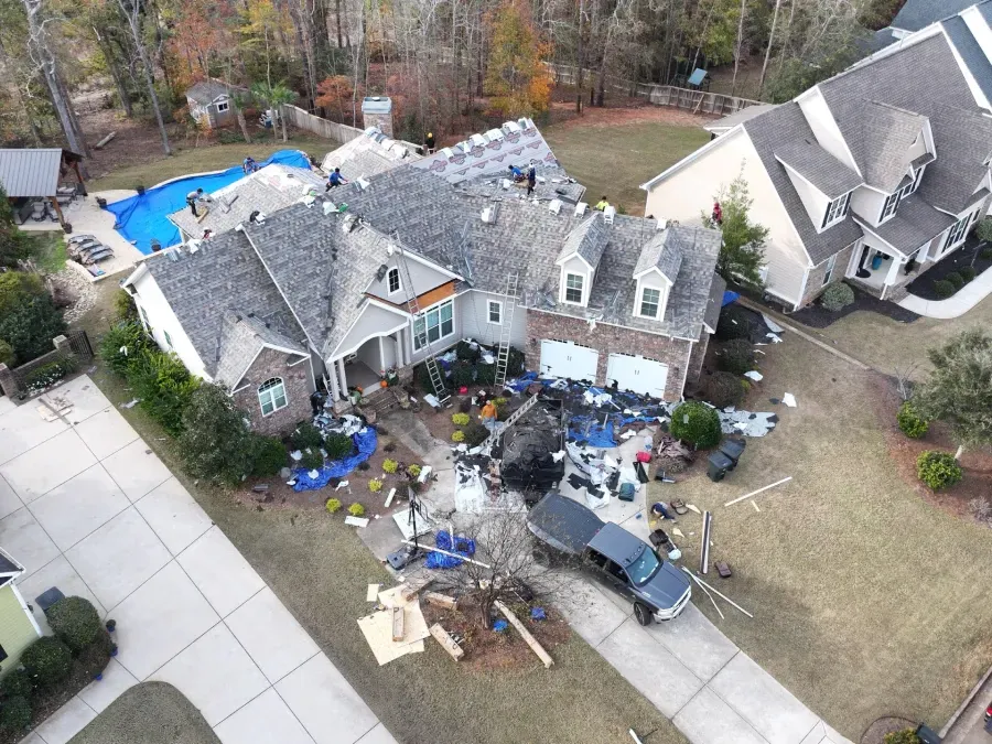 Aerial view of a house with roof damage and debris in the yard, likely after a storm.