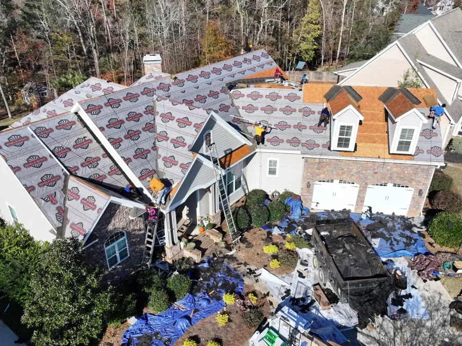House with severely damaged roof covered by blue tarp and scattered debris in the yard