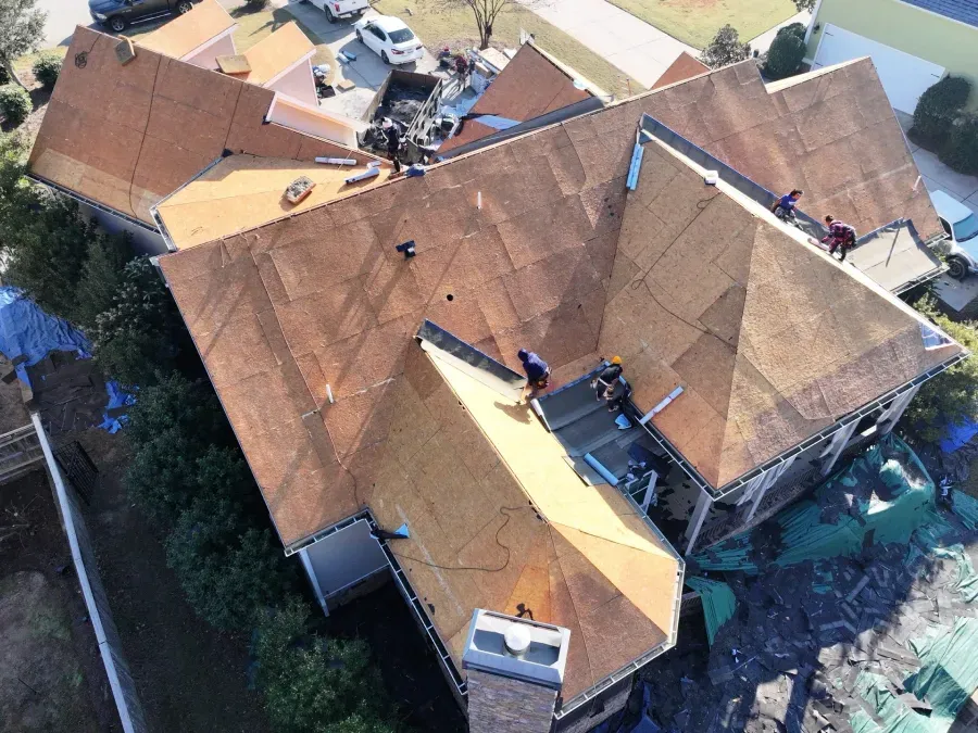Aerial view of a house with a tiled roof and people working on repairs above the property