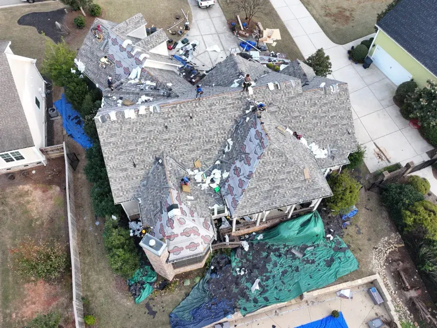 Aerial view of a storm-damaged house with missing roof sections and debris scattered around the yard