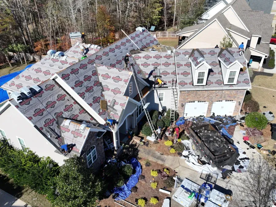 Aerial view of storm-damaged houses with torn roofs and debris scattered in the yard.