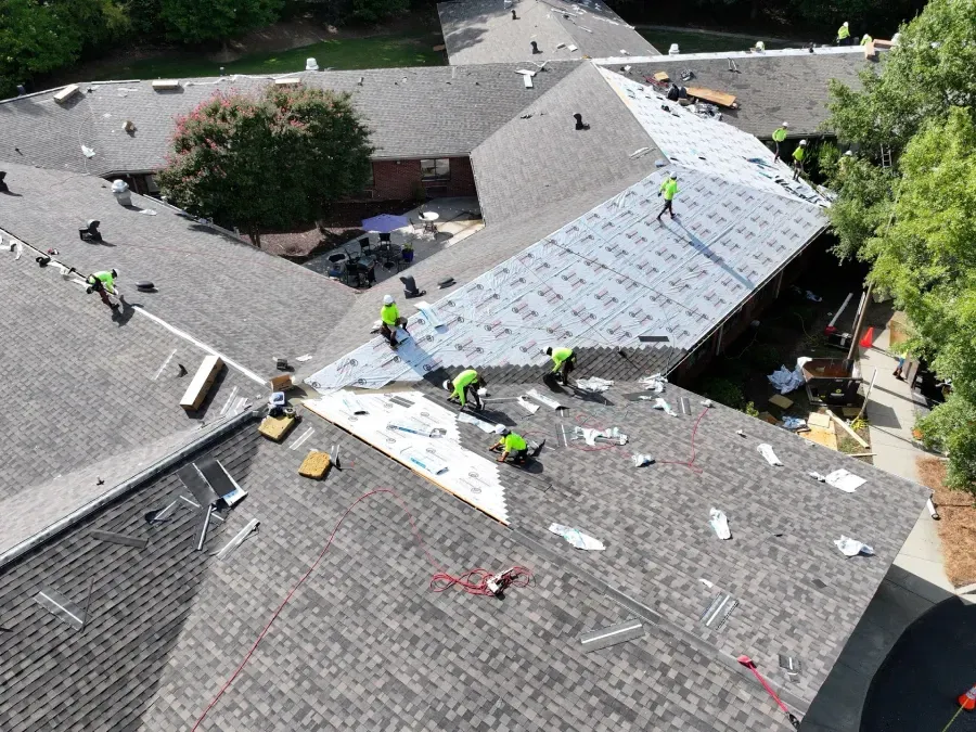 Workers repairing a roof with bright safety vests on a large building after storm damage