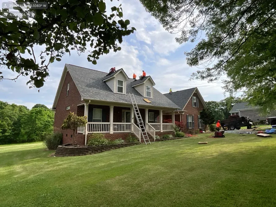 Brick house with gray roof and porch on a green lawn, framed by trees on a cloudy day