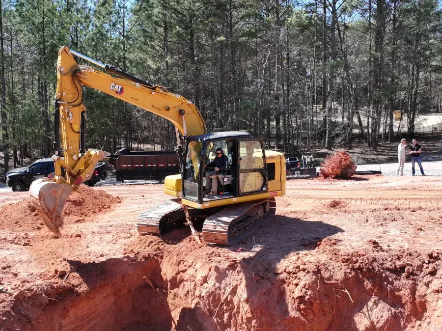 Yellow excavator digging a deep trench at a construction site with trees in the background