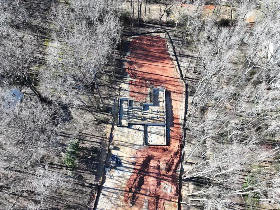 Aerial view of a red dirt path through trees with a small building centered near the bottom.