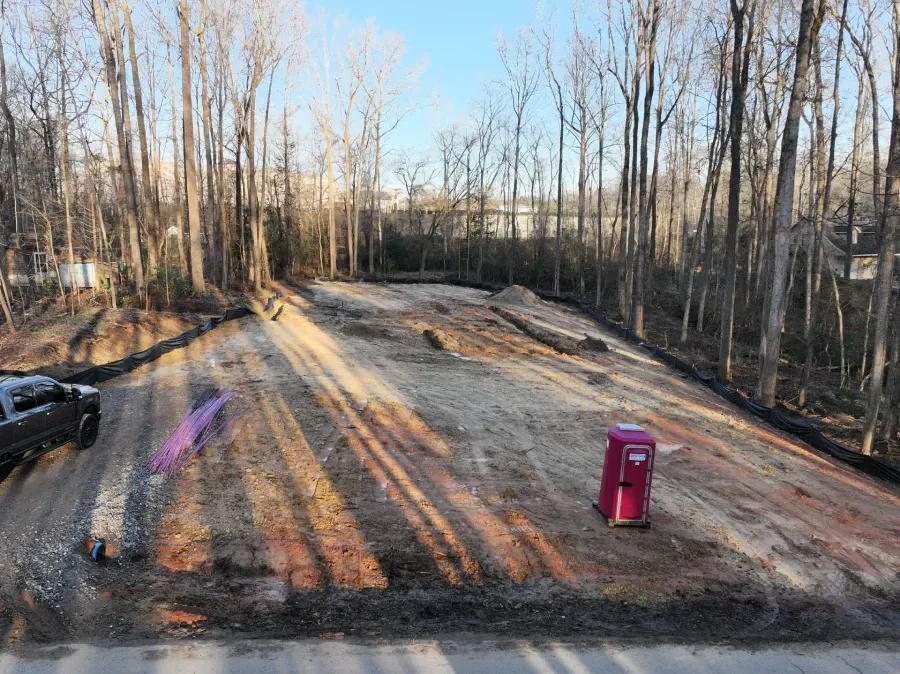 Bare dirt road in a wooded area, with a parked truck and a red mailbox post in early morning light