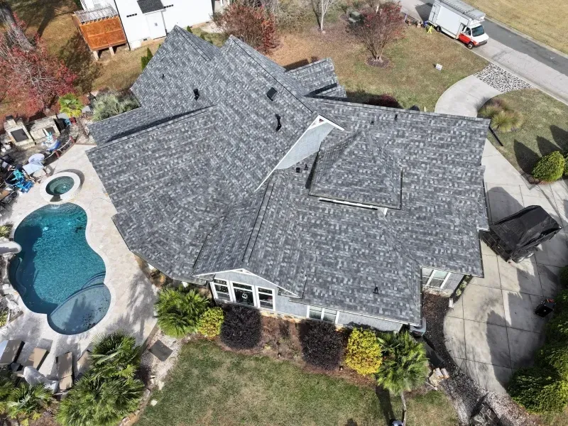Aerial view of a house with a gray roof, curved backyard pool, and landscaped yard