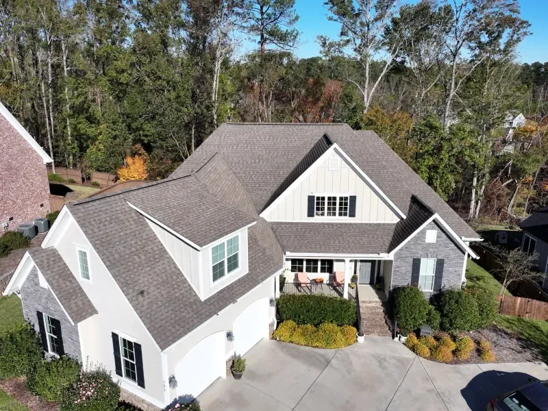 Aerial view of a white suburban house with a gray roof, front porch, and landscaped yard.