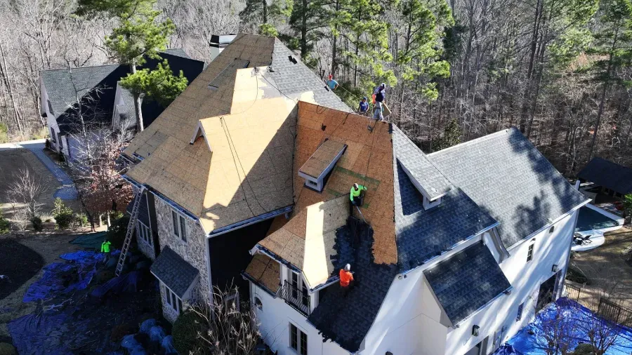 Aerial view of a house roof under construction, with workers and surrounding trees.