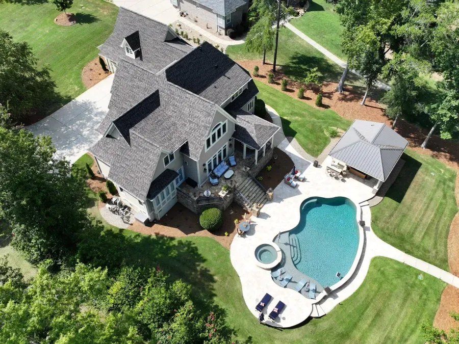 Aerial view of a large gray house with a backyard pool, patio, and white gazebo surrounded by trees.